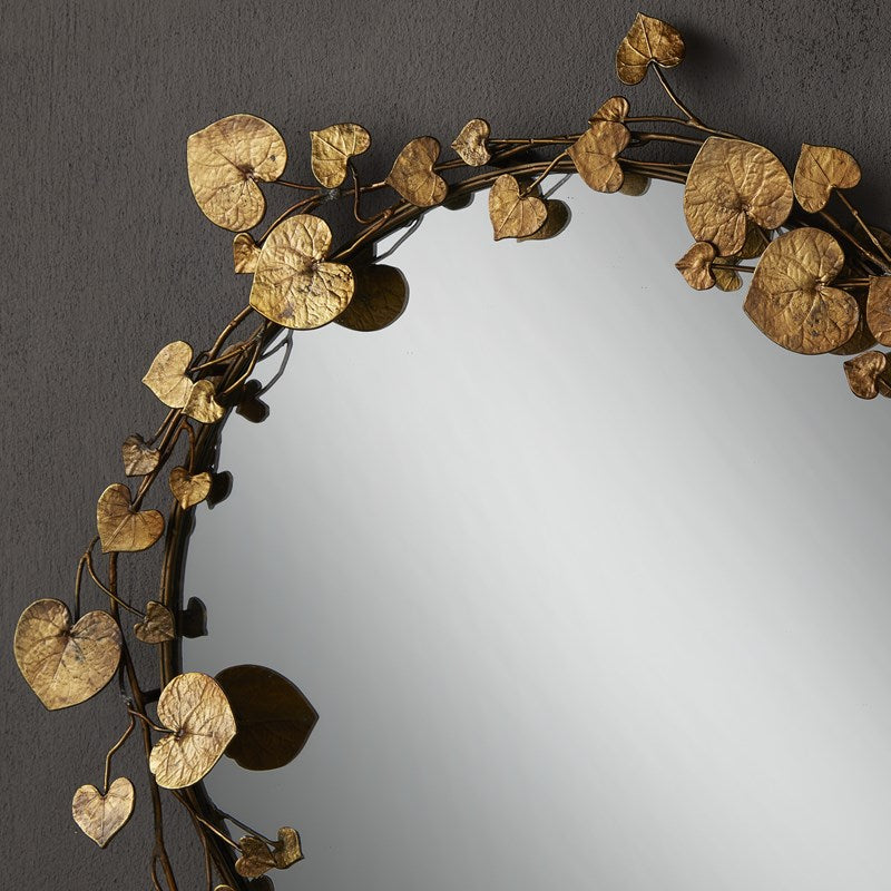 A close up image of the Vinna Brass Round Mirror by Currey & Company with a dark background truly showcasing the antique brass finish.  